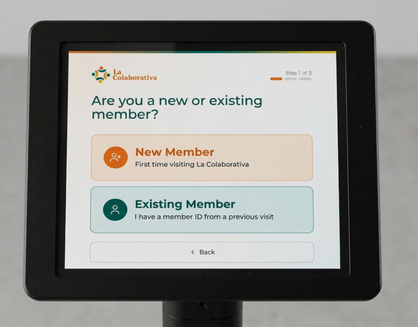 The La Colaborativa check-in kiosk on its stand, showing the screen "Are you a new or existing member?" with New Member and Existing Member buttons